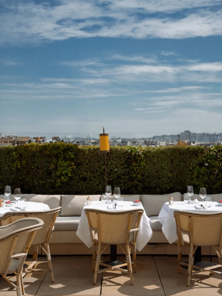 Terrace banquette and rattan chairs above a hedge with the Paris skyline at Girafe Paris