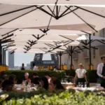 Busy terrace of diners under white parasols with the Eiffel Tower behind at Girafe Paris