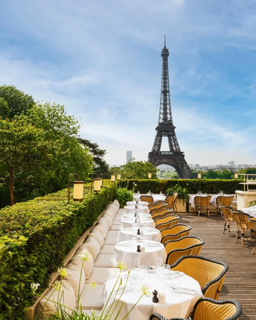 Long white-clothed terrace tables and rattan chairs facing the Eiffel Tower at Girafe Paris