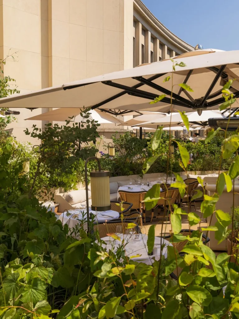 Terrace tables framed by lush planting and parasols beside the Palais at Girafe Paris