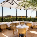 Rattan chairs and white-clothed tables under large parasols behind a hedge at Girafe Paris