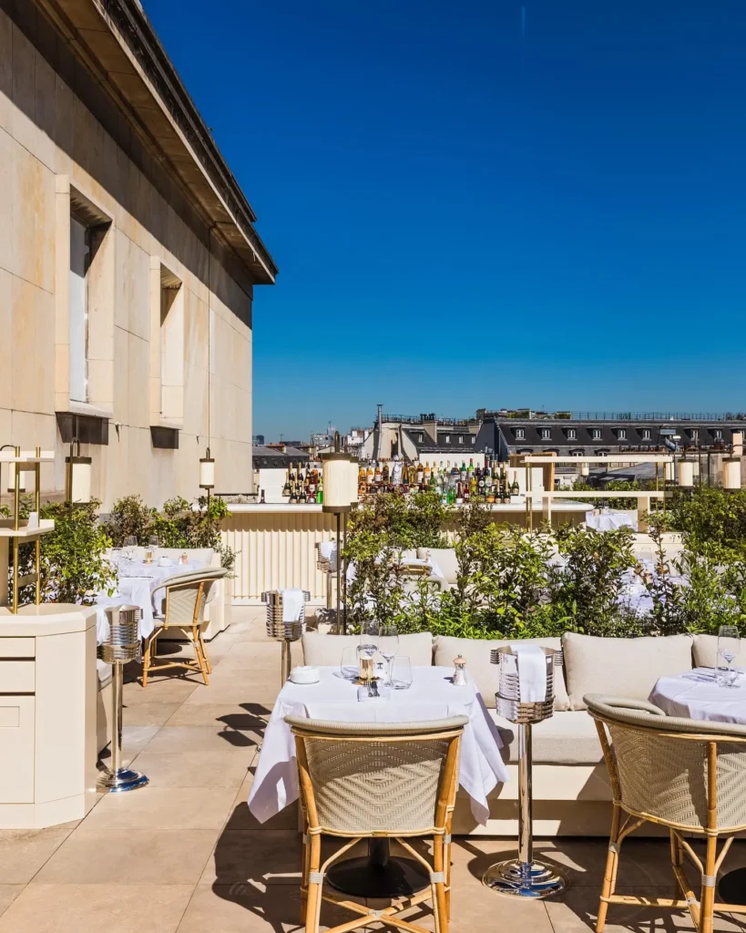Rooftop terrace with an outdoor bar and set tables over the Paris rooftops at Girafe Paris
