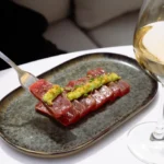 Sliced raw tuna with avocado and herbs on a speckled plate beside white wine at Girafe Paris