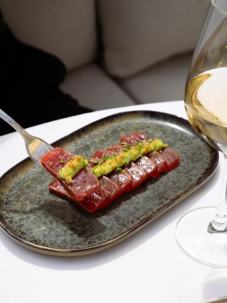 Sliced raw tuna with avocado and herbs on a speckled plate beside white wine at Girafe Paris