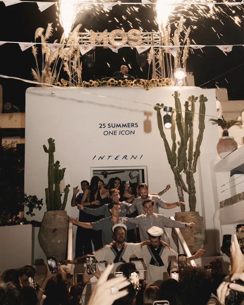 Staff posing with sparklers under the MOS sign and a 25 Summers One Icon wall at Interni Restaurant Mykonos