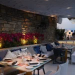 Stone-wall banquette set for dinner with lit bougainvillea at dusk at Interni Restaurant Mykonos