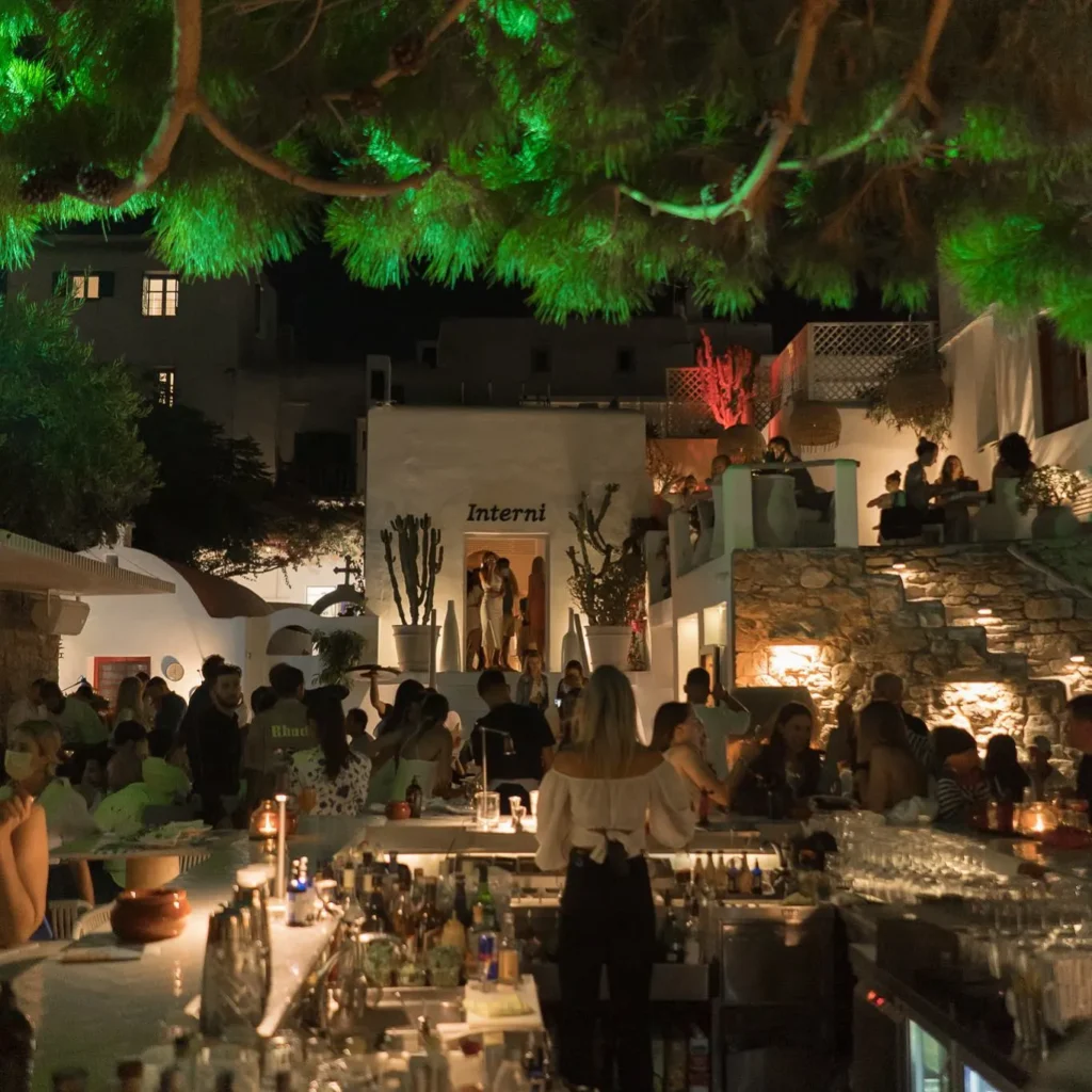 Busy central bar beneath a green-lit pine at night at Interni Restaurant Mykonos