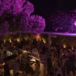Crowded bar under purple-lit trees at night at Interni Restaurant Mykonos