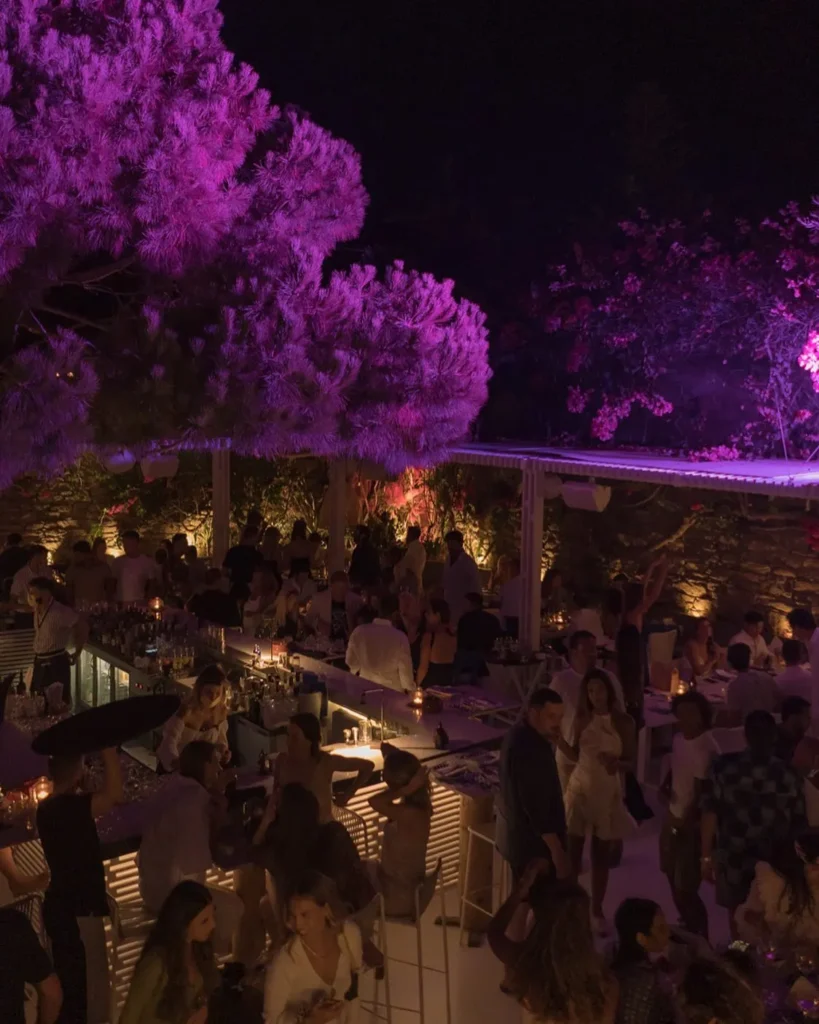 Crowded bar under purple-lit trees at night at Interni Restaurant Mykonos