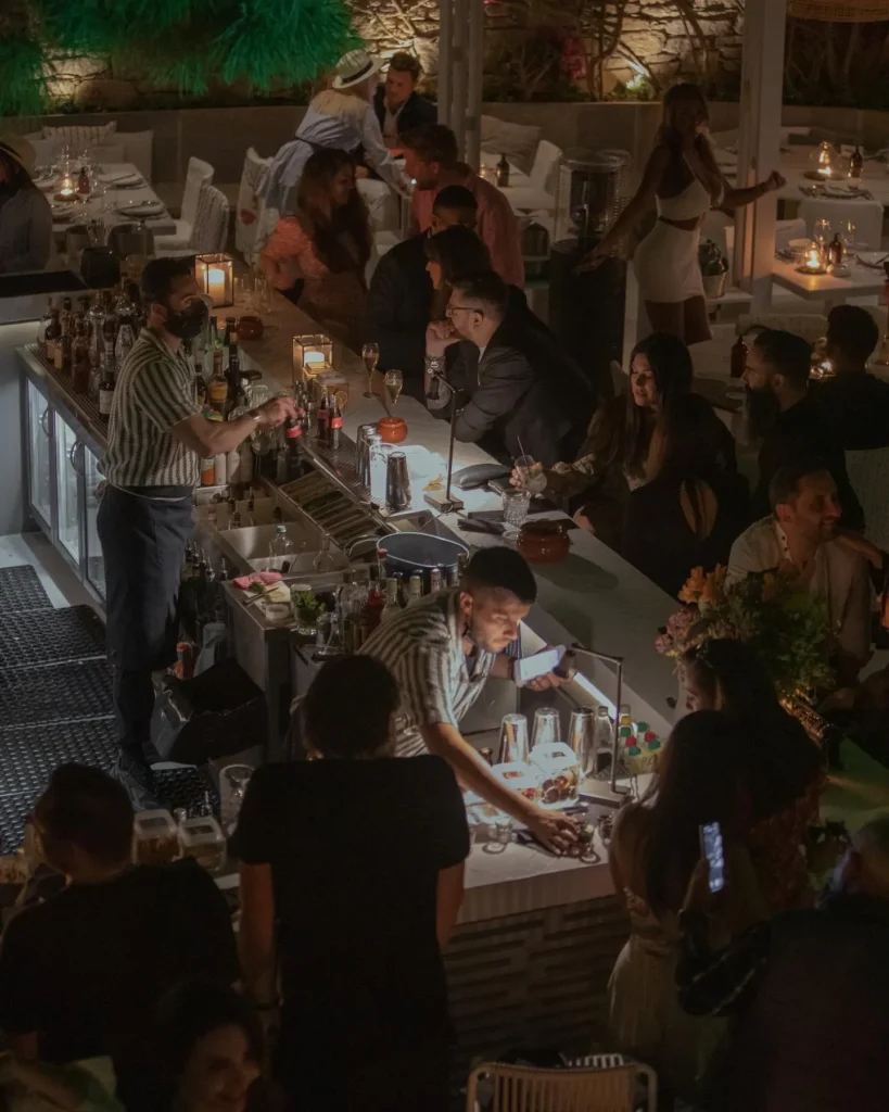 Bartenders mixing drinks behind the bar as guests gather at night at Interni Restaurant Mykonos