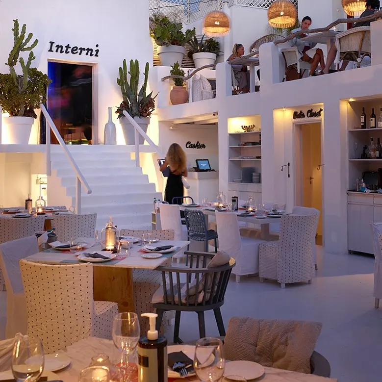 Whitewashed dining area with set tables, the Interni sign and stairs at Interni Restaurant Mykonos