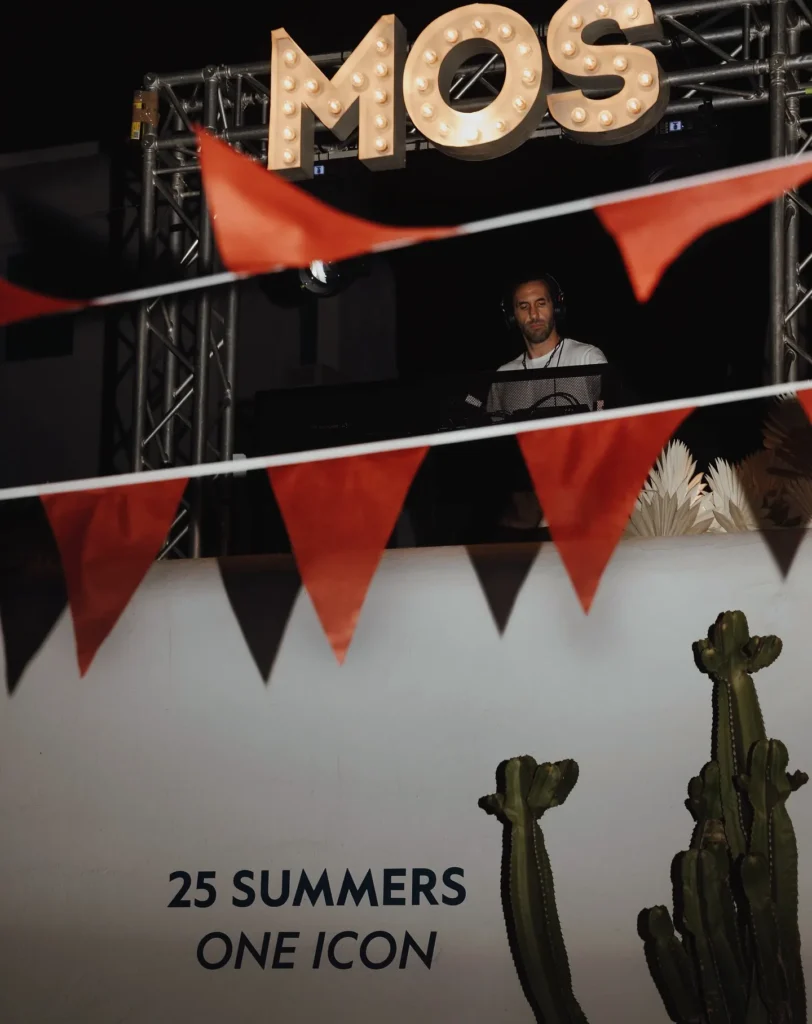 DJ playing beneath an illuminated MOS sign framed by bunting at Interni Restaurant Mykonos