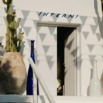 INTERNI doorway framed by cacti, a blue bottle and a terracotta urn in golden light at Interni Restaurant Mykonos