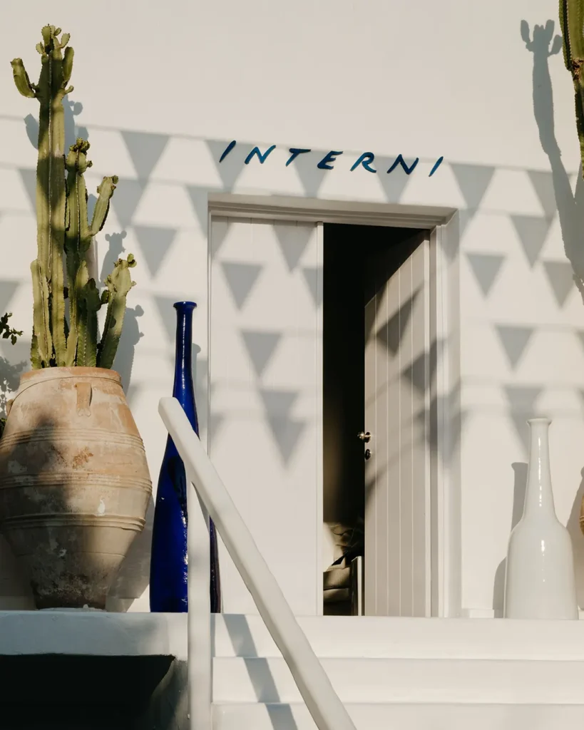 INTERNI doorway framed by cacti, a blue bottle and a terracotta urn in golden light at Interni Restaurant Mykonos
