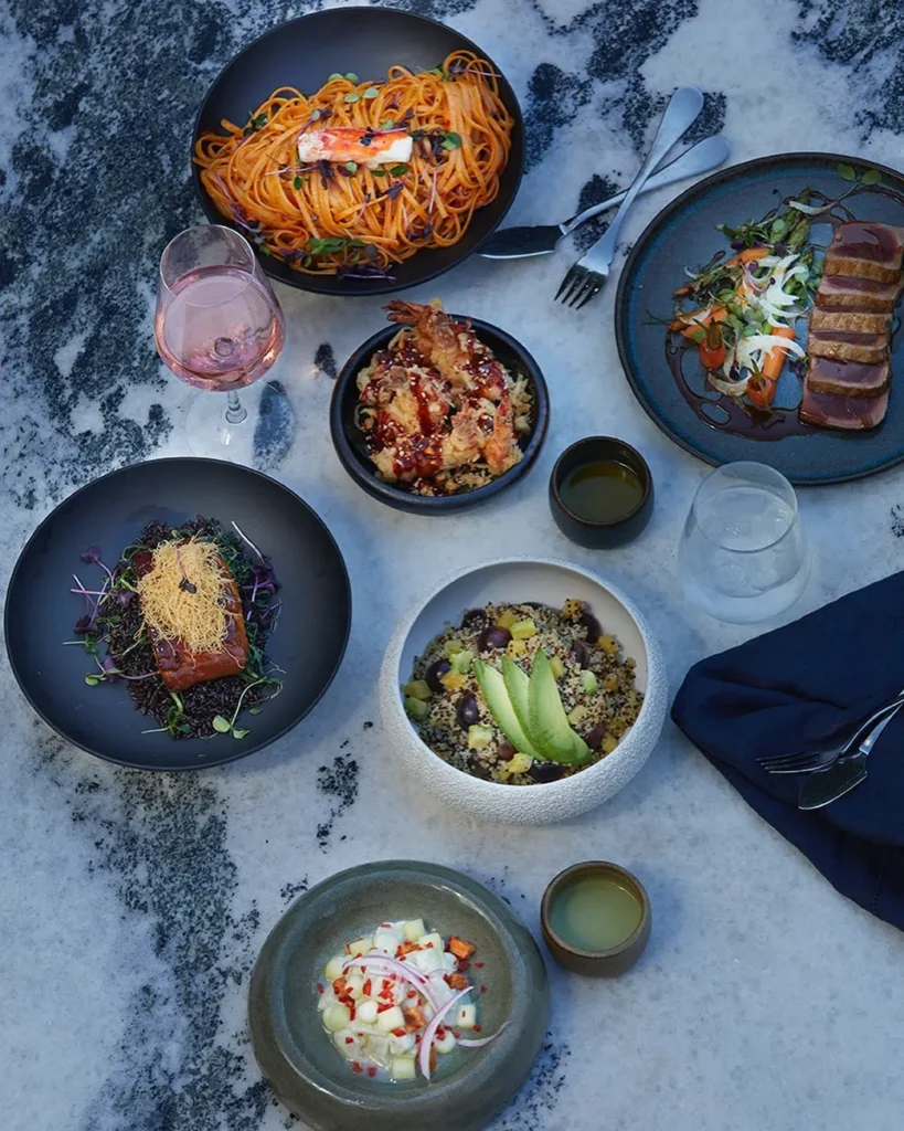 Spread of pasta, seared tuna, salmon and grain bowls on a marble surface at Interni Restaurant Mykonos