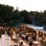 Elevated view of the busy dining terraces and bar surrounded by trees at dusk at Interni Restaurant Mykonos