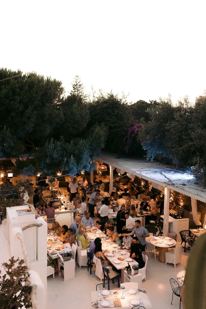 Elevated view of the busy dining terraces and bar surrounded by trees at dusk at Interni Restaurant Mykonos