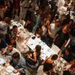 Overhead view of a packed dinner party across long white tables at Interni Restaurant Mykonos