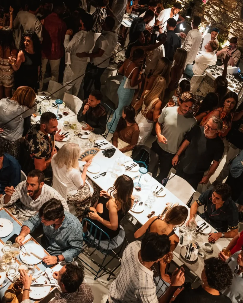 Overhead view of a packed dinner party across long white tables at Interni Restaurant Mykonos