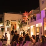 Guests dining beneath the lit Interni sign amid coloured lighting at night at Interni Restaurant Mykonos