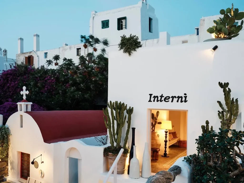 Interni sign on a whitewashed wall beside a chapel and cacti at dusk at Interni Restaurant Mykonos