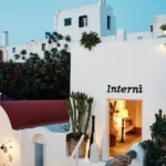 Interni sign on a whitewashed wall beside a chapel and cacti at dusk at Interni Restaurant Mykonos