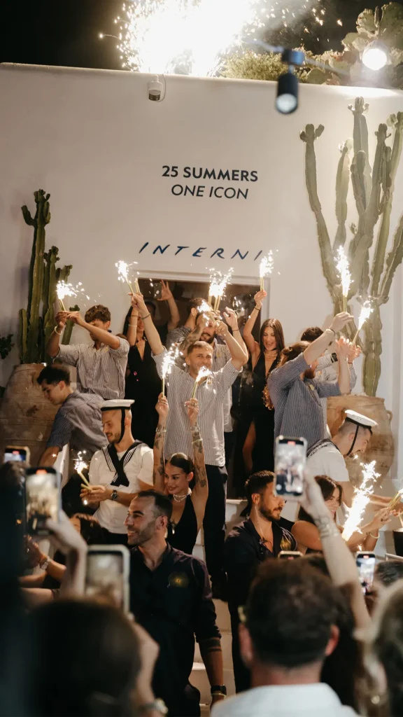 Team raising sparklers before the 25 Summers One Icon wall at Interni Restaurant Mykonos