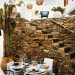 Round table laid with dishes beside a stone staircase and cactus at Interni Restaurant Mykonos