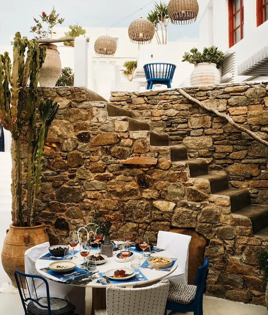 Round table laid with dishes beside a stone staircase and cactus at Interni Restaurant Mykonos
