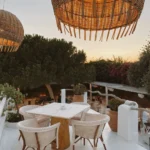 Marble table and woven chairs under large rattan pendant lamps at sunset at Interni Restaurant Mykonos