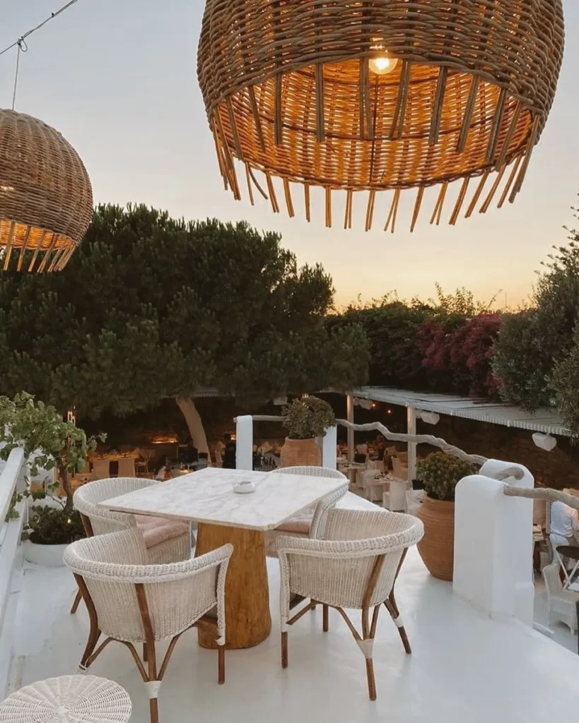 Marble table and woven chairs under large rattan pendant lamps at sunset at Interni Restaurant Mykonos