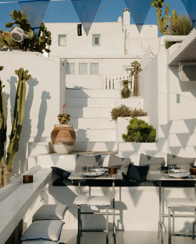 Cushioned corner banquette and high tables among cacti and whitewashed steps at Interni Restaurant Mykonos