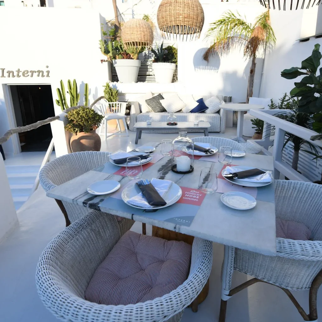 Marble table and woven chairs beside a cushioned sofa and cacti at Interni Restaurant Mykonos