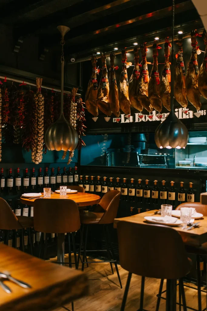 Dining room with tan chairs, brass pendants and rows of hanging jamón and wine at La Bodeguilla Palma