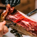Gloved hand carving thin slices from a leg of Iberian jamón at La Bodeguilla Palma