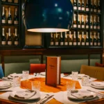 Set round table with a wine list under a large blue globe lamp before a cava-bottle wall at La Bodeguilla Palma