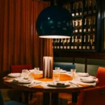 Round table under a blue globe lamp beside a champagne-bottle wall and rust curtain at La Bodeguilla Palma