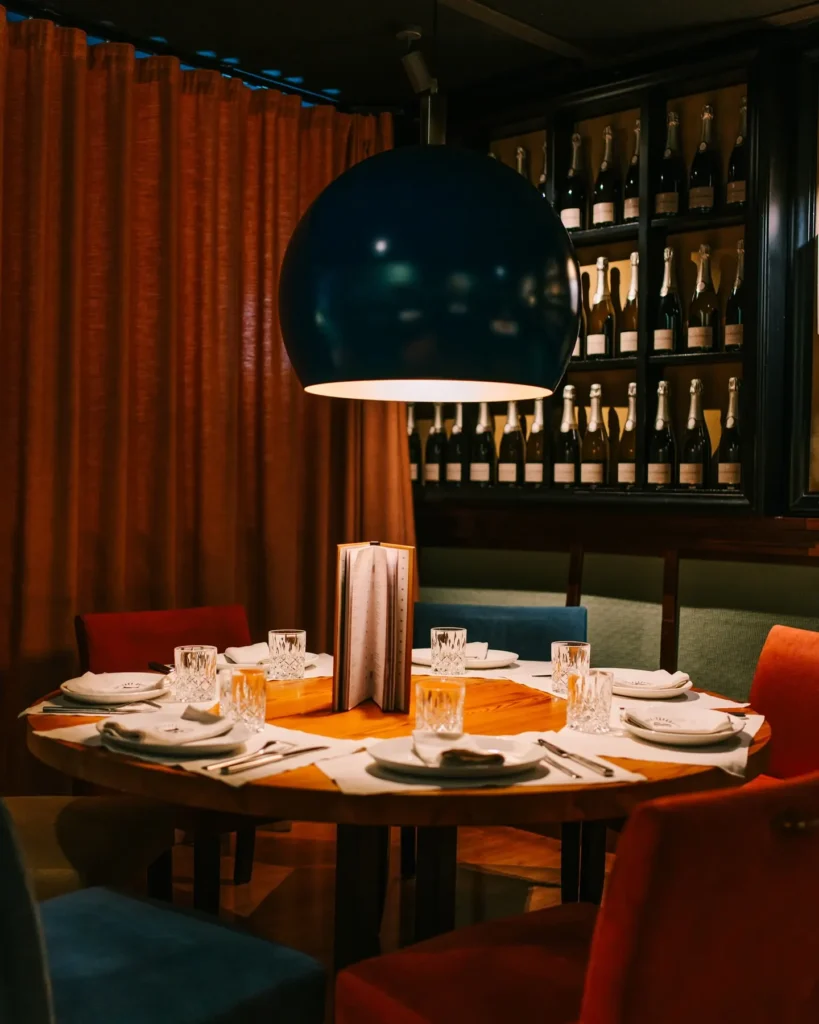 Round table under a blue globe lamp beside a champagne-bottle wall and rust curtain at La Bodeguilla Palma