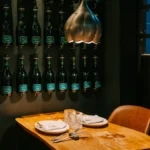 Live-edge table under a brass tulip lamp against a wall of Kripta cava bottles at La Bodeguilla Palma