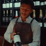 Server in a branded leather apron presenting a bottle of red wine at La Bodeguilla Palma