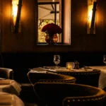 Velvet banquette table below a vase of red roses framed by alabaster sconces at L'Avenue Paris