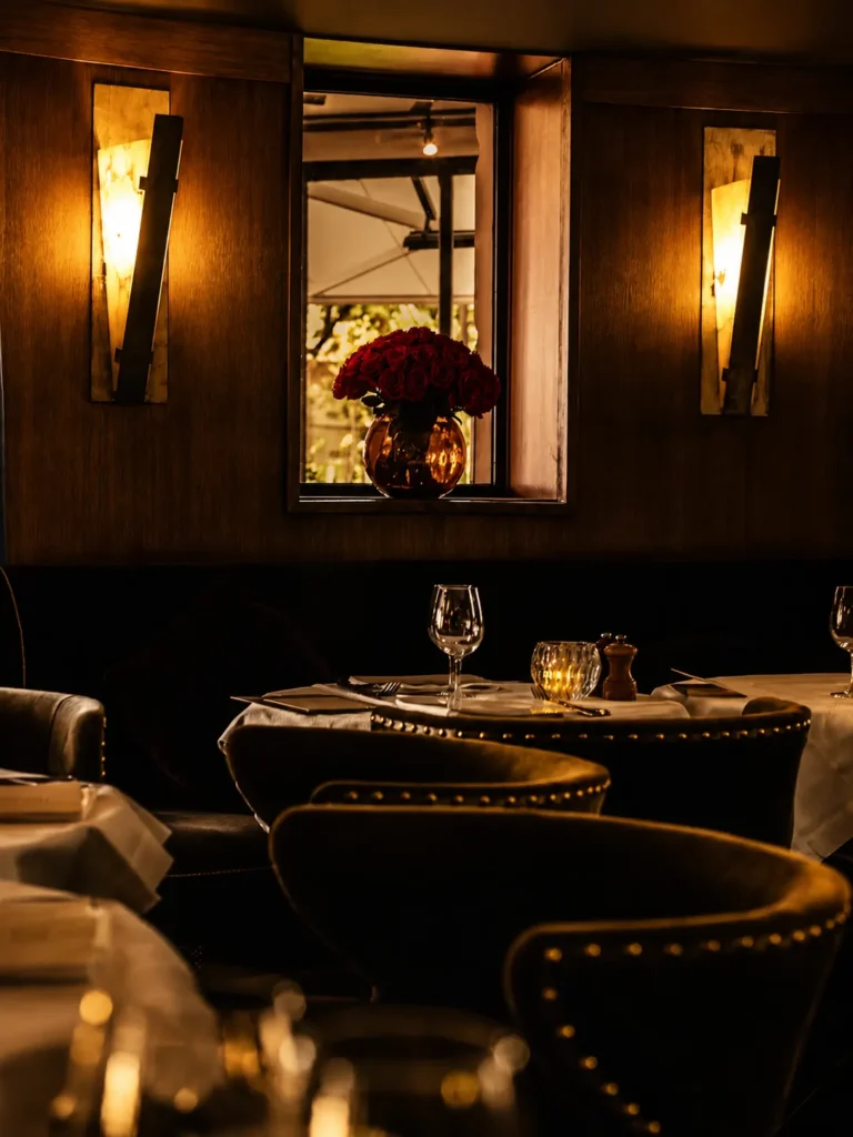 Velvet banquette table below a vase of red roses framed by alabaster sconces at L'Avenue Paris