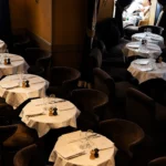 Candlelit dining room with white-clothed tables and dark velvet armchairs at L'Avenue Paris