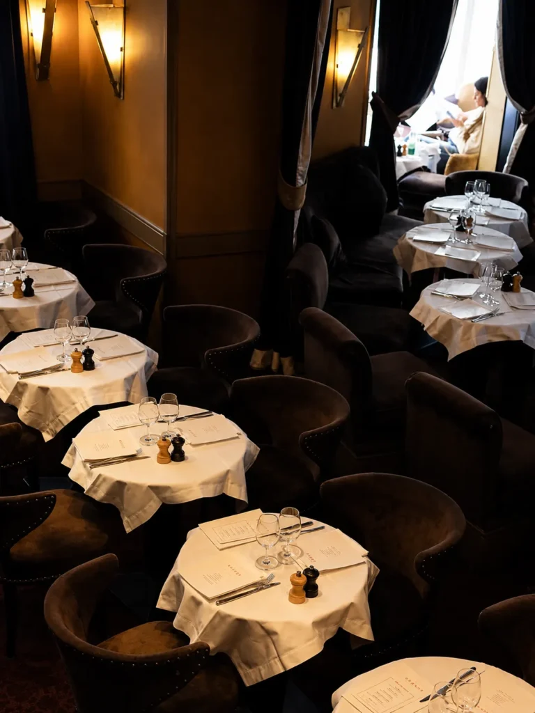 Candlelit dining room with white-clothed tables and dark velvet armchairs at L'Avenue Paris