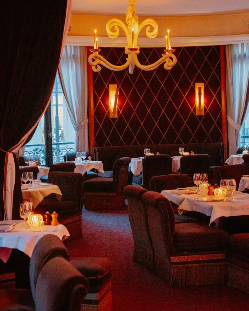 Dining room with a studded burgundy wall, sculptural white chandelier and dark velvet armchairs at lavenue Paris
