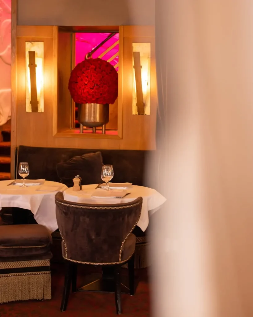Velvet banquette table below a ball of red roses framed by alabaster sconces at lavenue Paris