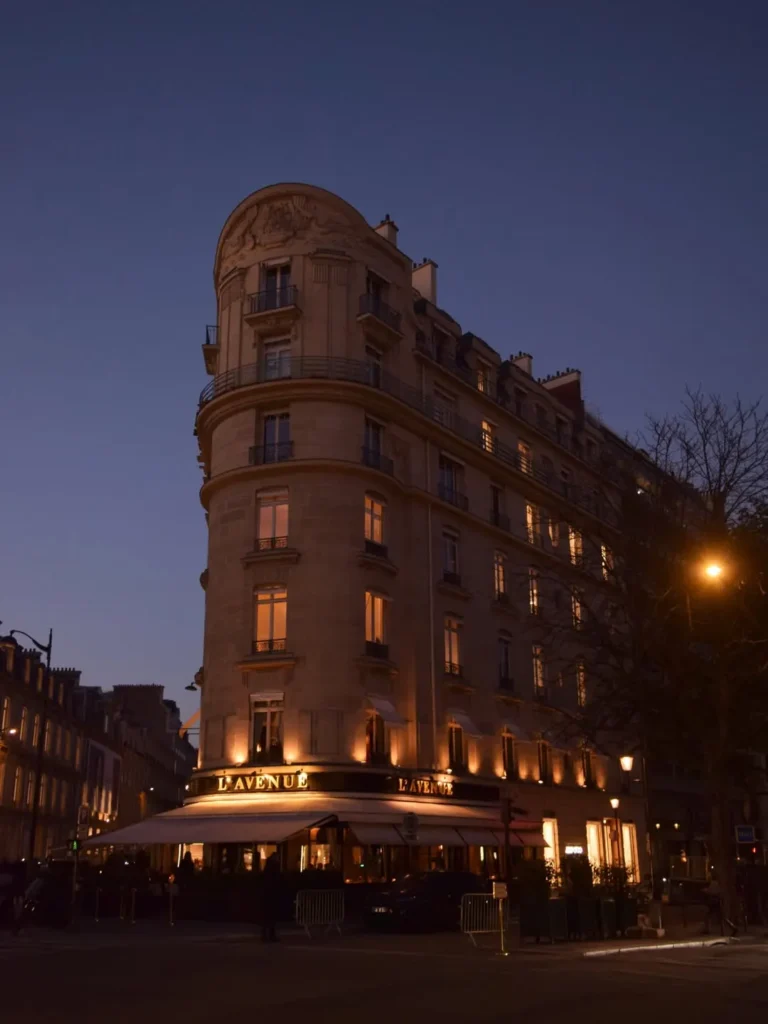 Full Haussmannian corner building glowing at twilight above the lavenue awning at lavenue Paris