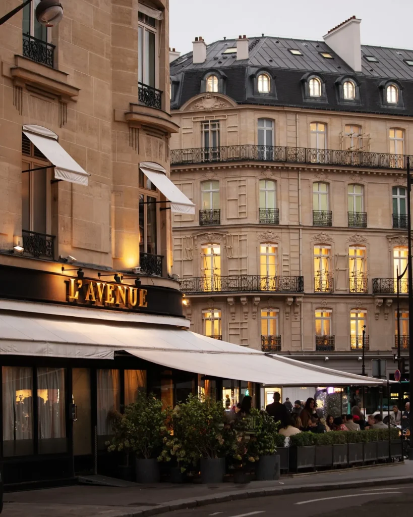 Gold lavenue sign above the awning and hedged terrace on Avenue Montaigne at dusk at lavenue Paris