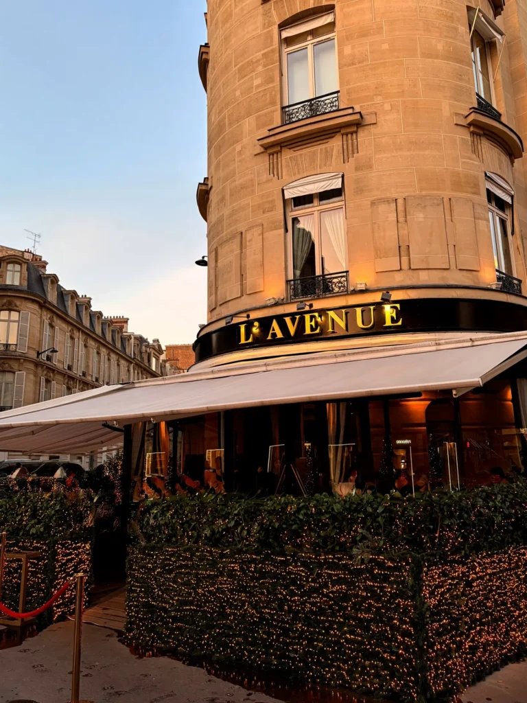 Gold lavenue sign and awning above a fairy-lit hedge in golden evening light at lavenue Paris