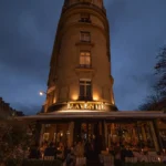 Rounded corner building lit at dusk with the lavenue sign over the candlelit terrace at lavenue Paris